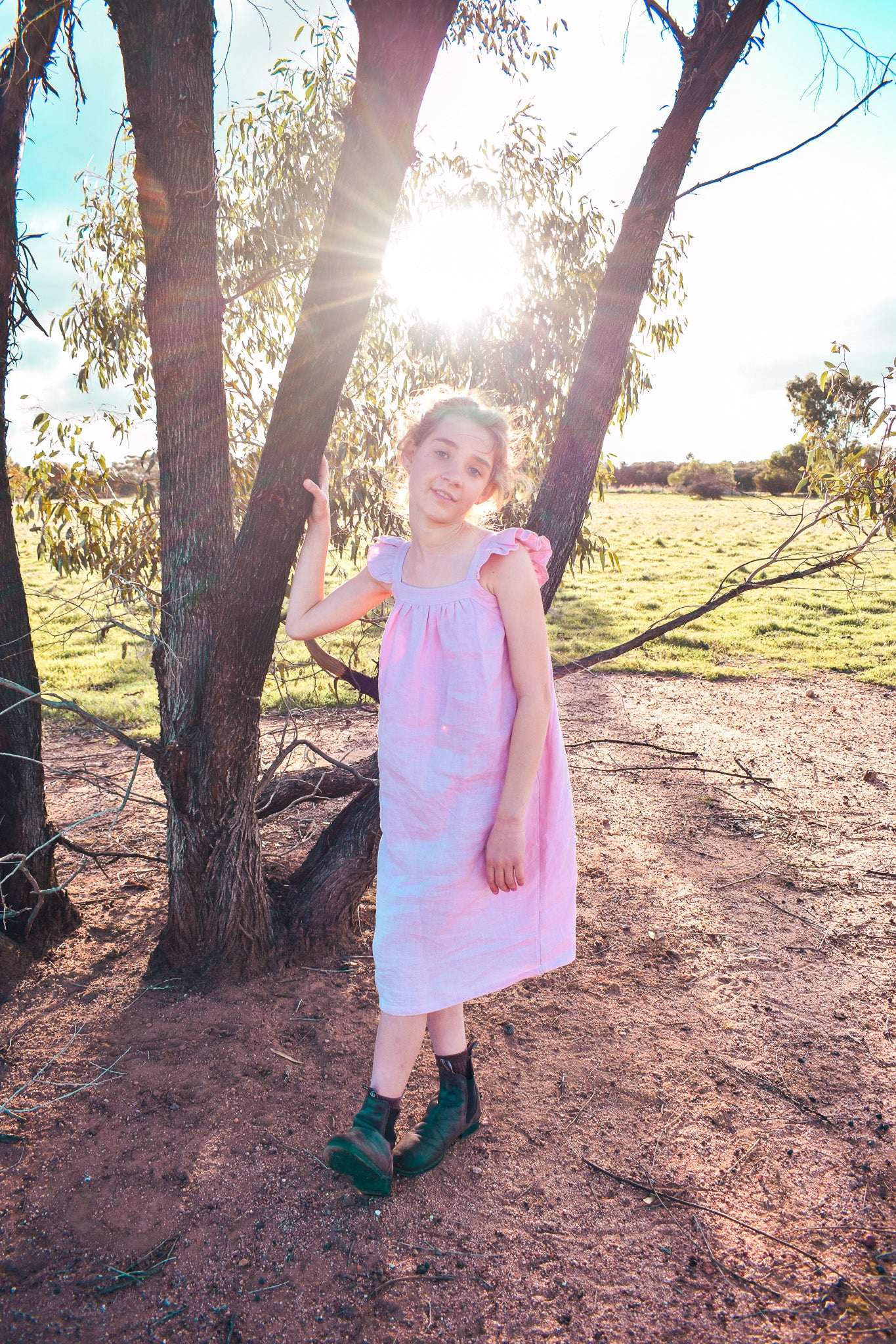 Young girl in a pink linen dress standing in a natural setting with trees and open field.