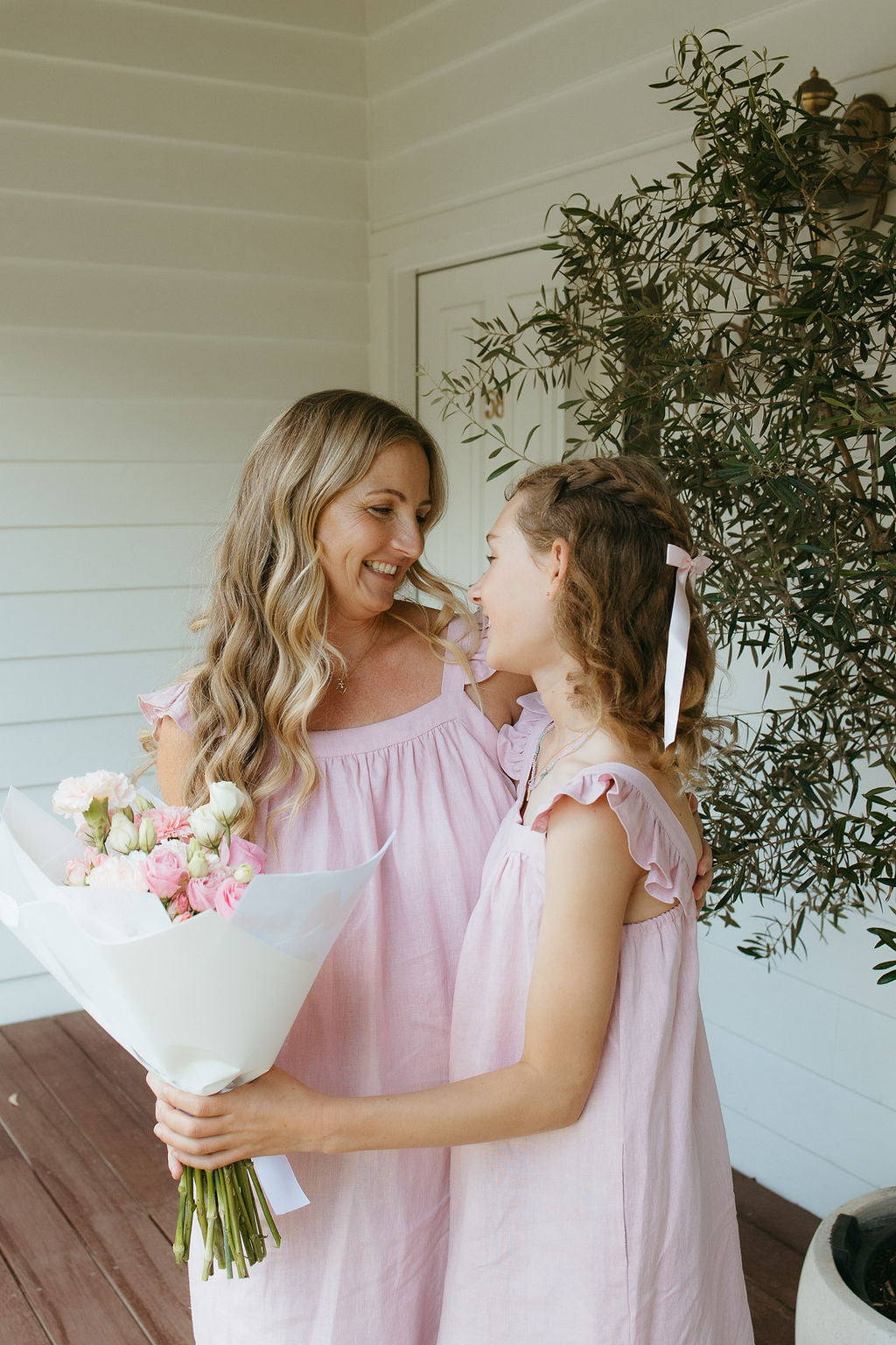 Woman and young girl in pink matching linen dresses holding flowers outside