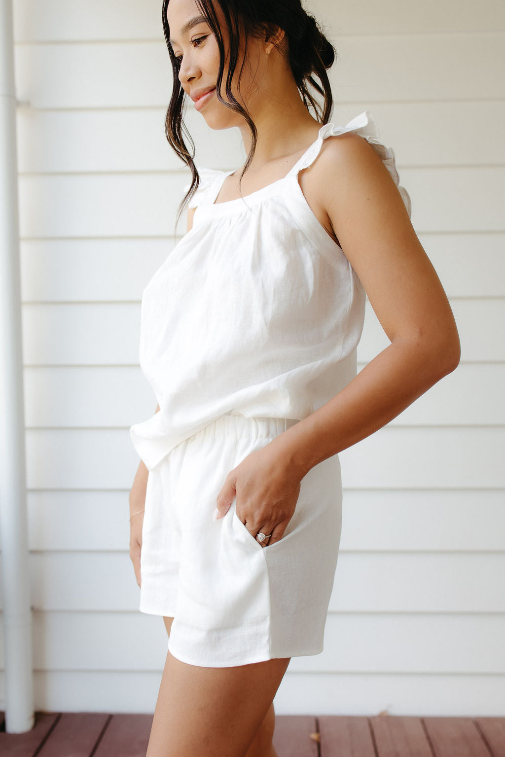 Woman wearing a white linen top and shorts against a white wall.