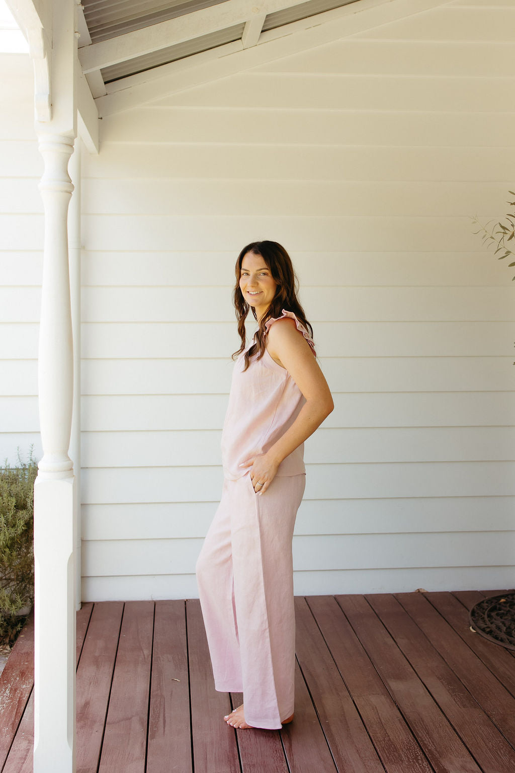 Woman in a pink linen sleep set standing on a wooden deck with a white house in the background
