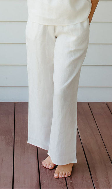 Woman in a white linen sleep set standing on a wooden deck with a white wall background