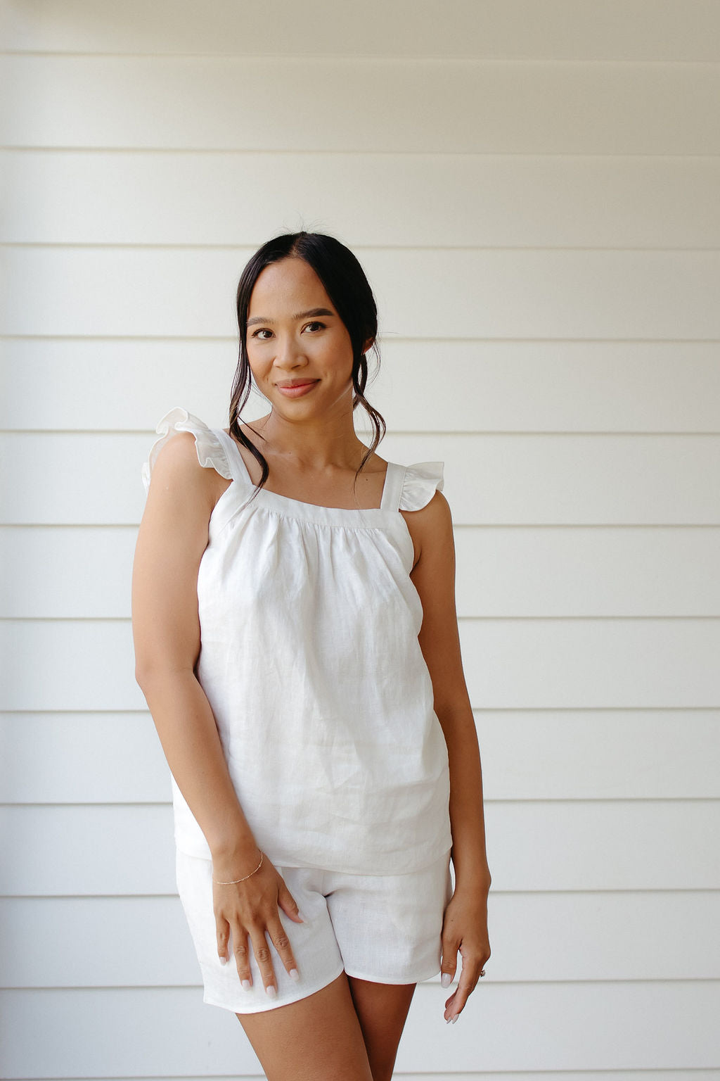 Woman wearing white linen sleepwear sleeveless top and shorts against a white background