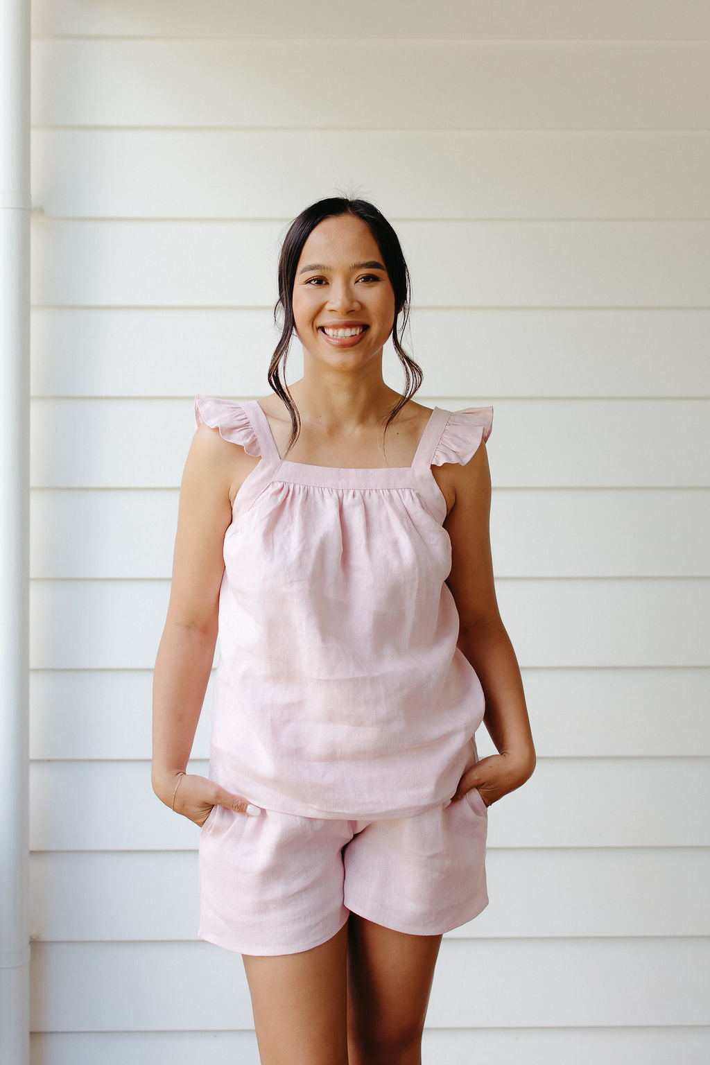 Woman wearing a pink linen top and shorts set against a white wooden background