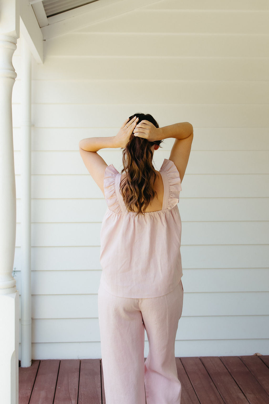 Woman in a pink linen set standing on a wooden deck with white walls.