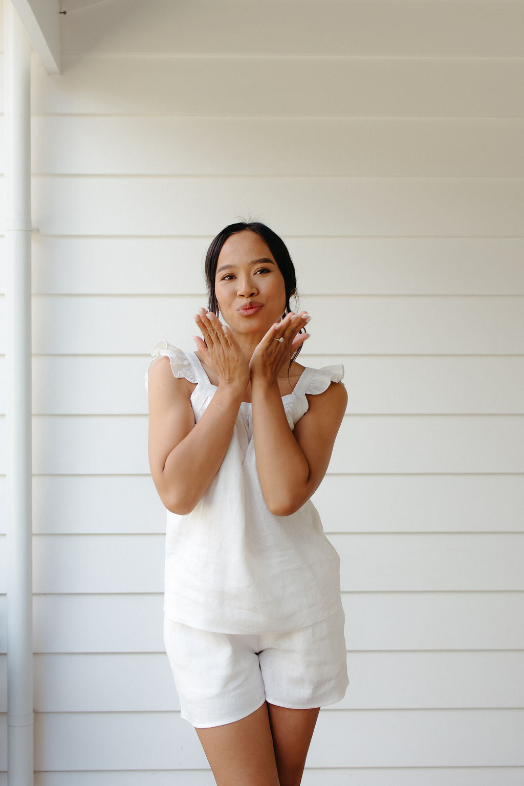 Woman in white linen sleepwear standing against a white wall