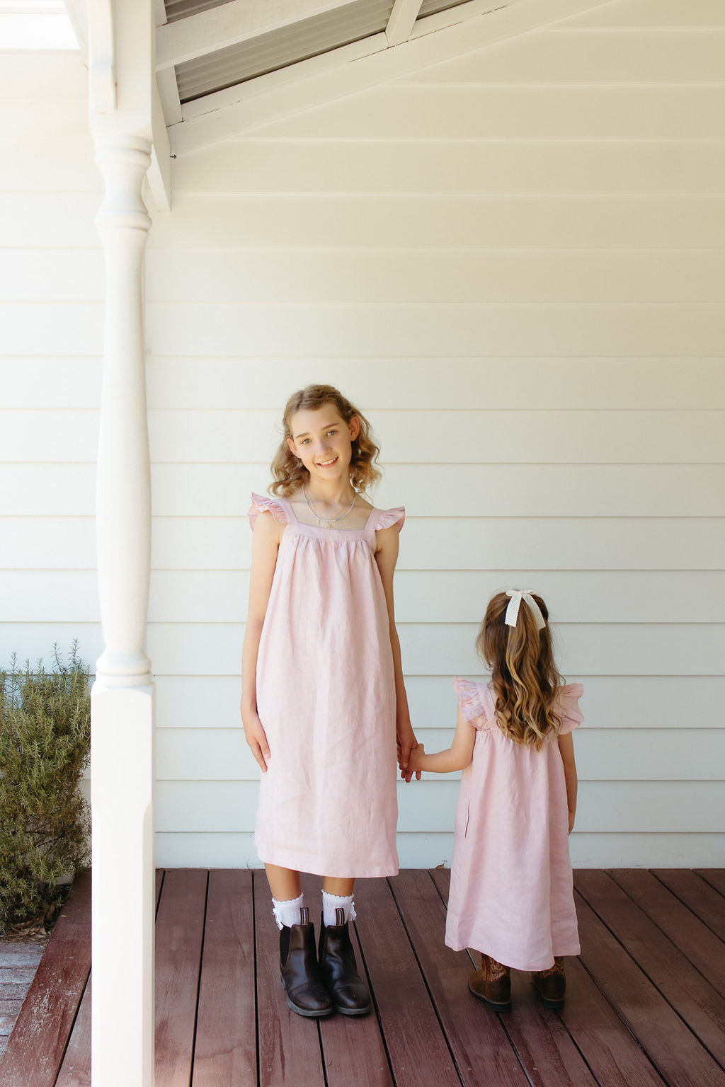 Two young girls in pink linen dresses standing on a wooden deck.